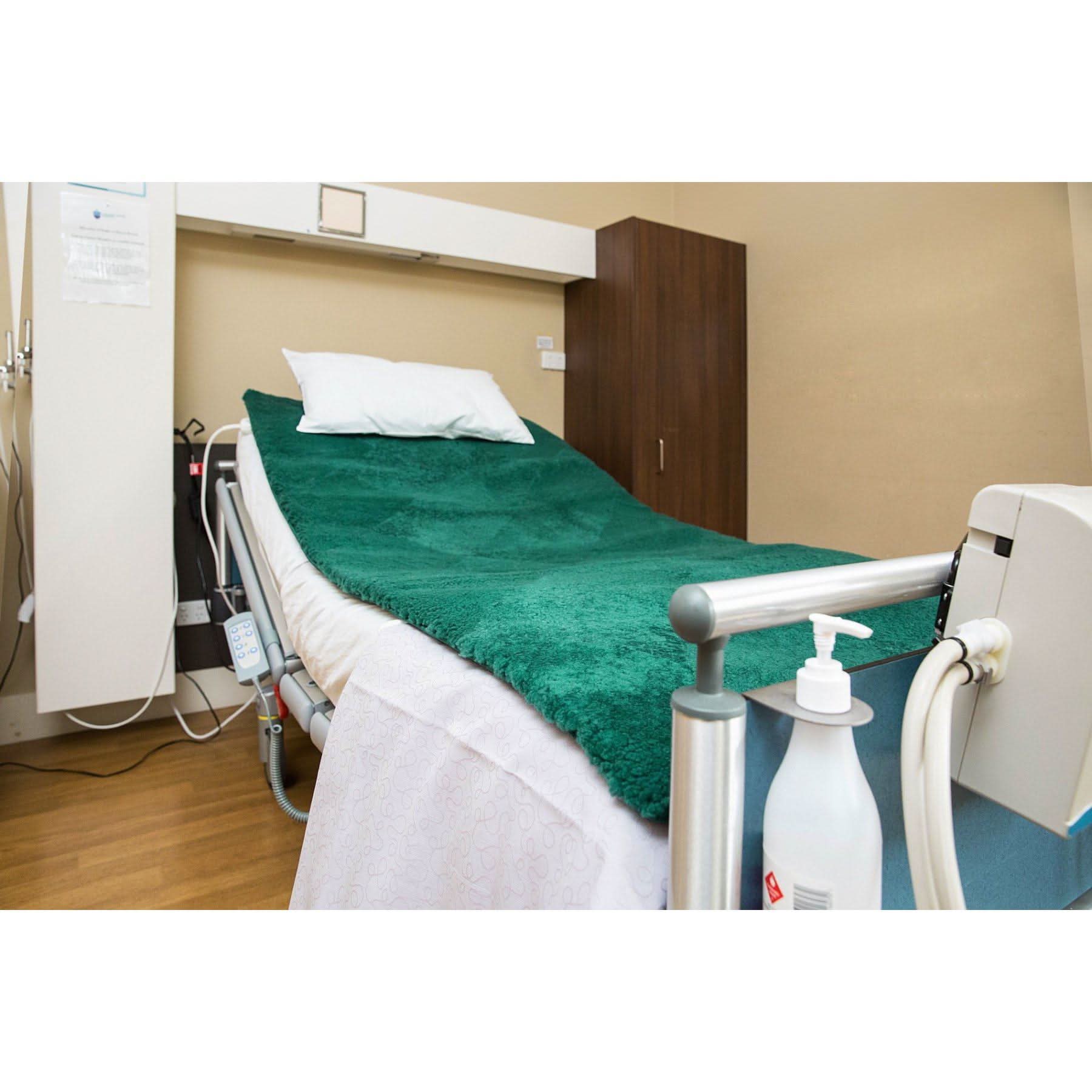 Green wool sheepskin bed cover on adjustable hospital bed in clinical setting. - Yellow Earth Australia