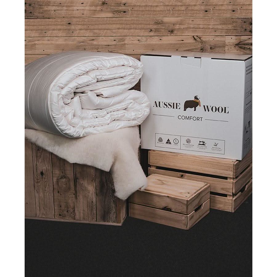 Rolled white wool doona displayed with packaging on wooden platform, overhead view. - Yellow Earth Australia