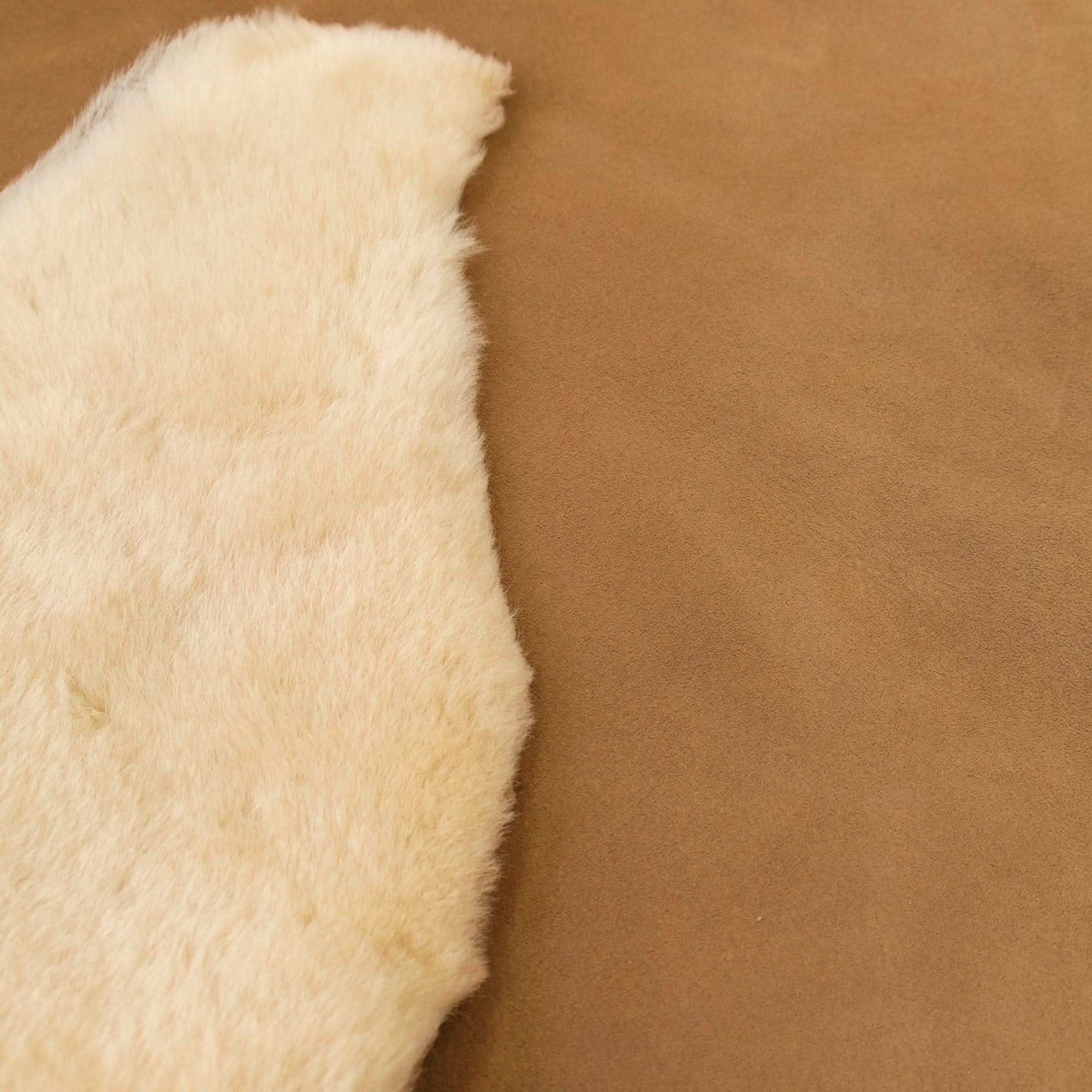 Natural cream sheepskin rug with soft wool pile on tan background, side view. - Yellow Earth Australia