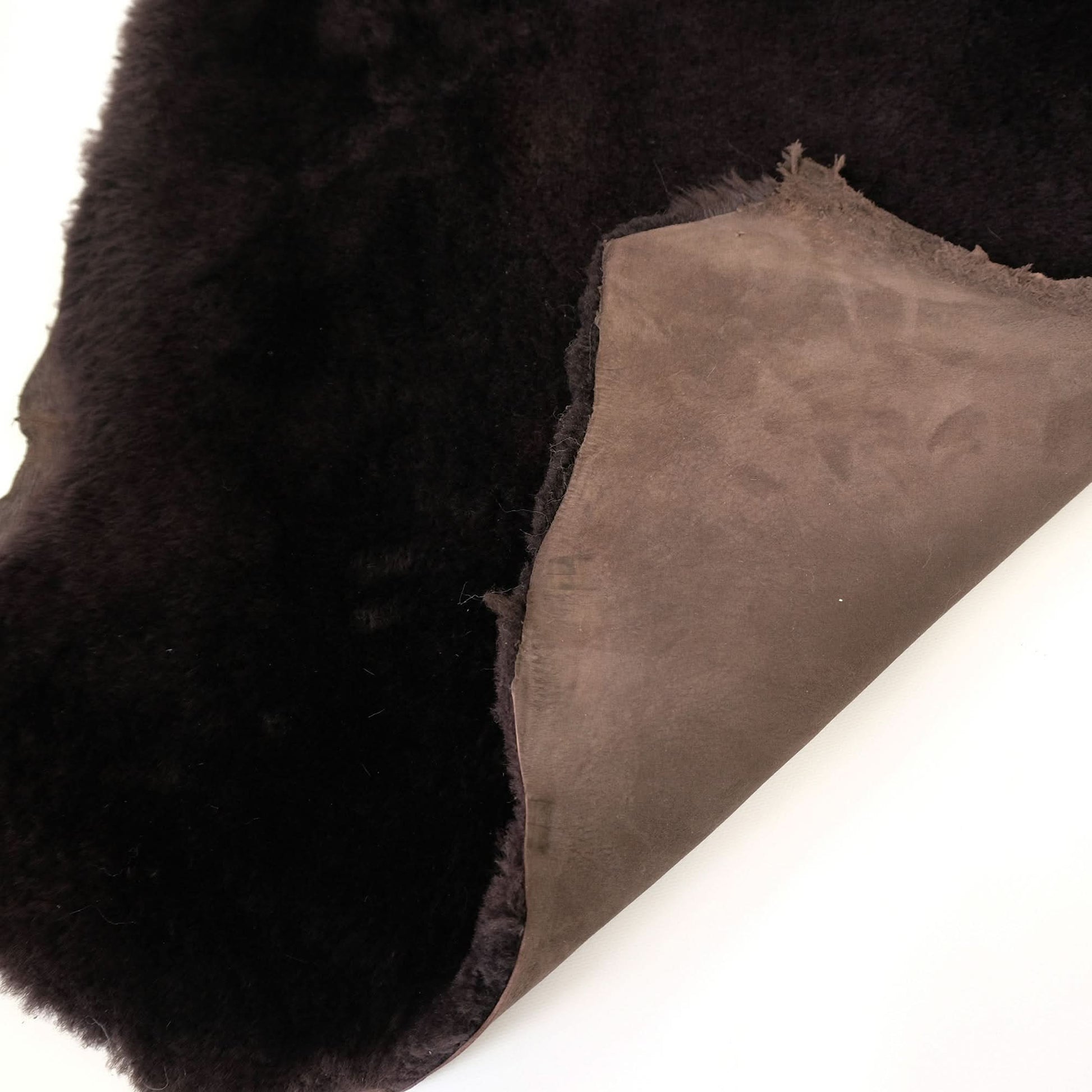 Black sheepskin rug with suede backing displayed at an angle showing texture and pile. - Yellow Earth Australia
