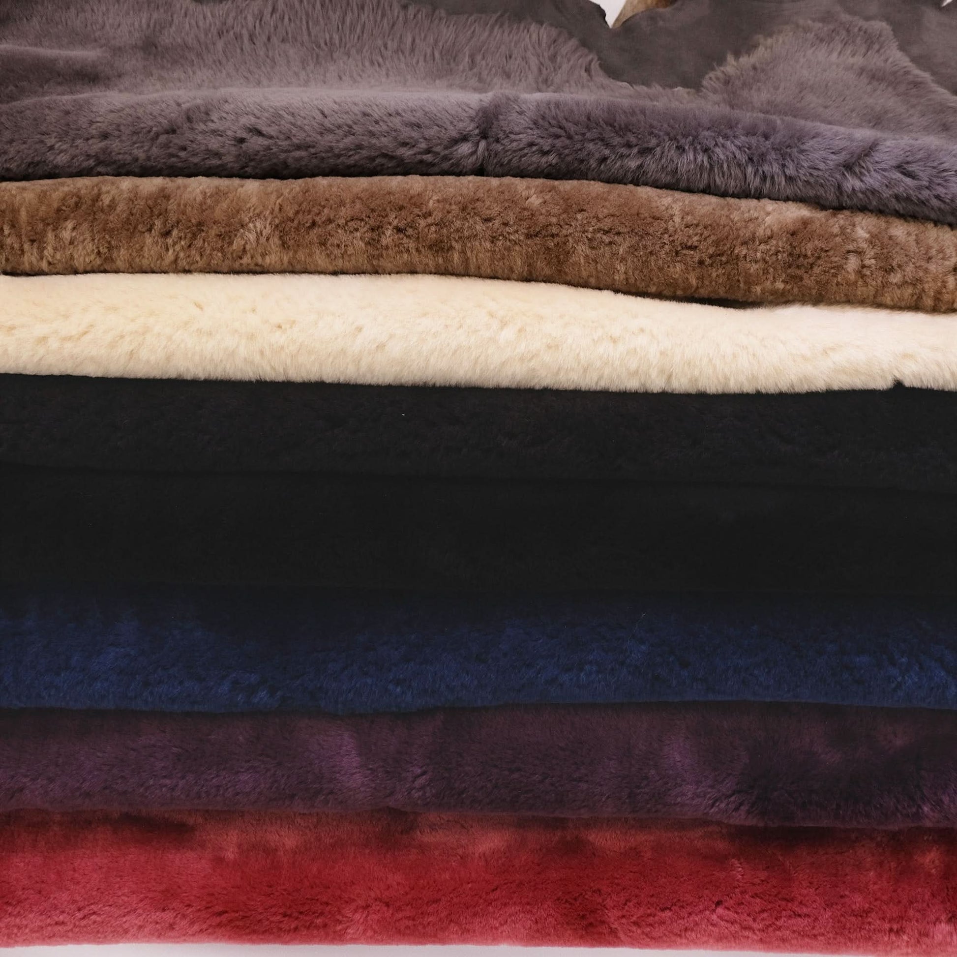 Stack of soft sheepskin rugs in grey, tan, cream, black, navy and red colours. - Yellow Earth Australia
