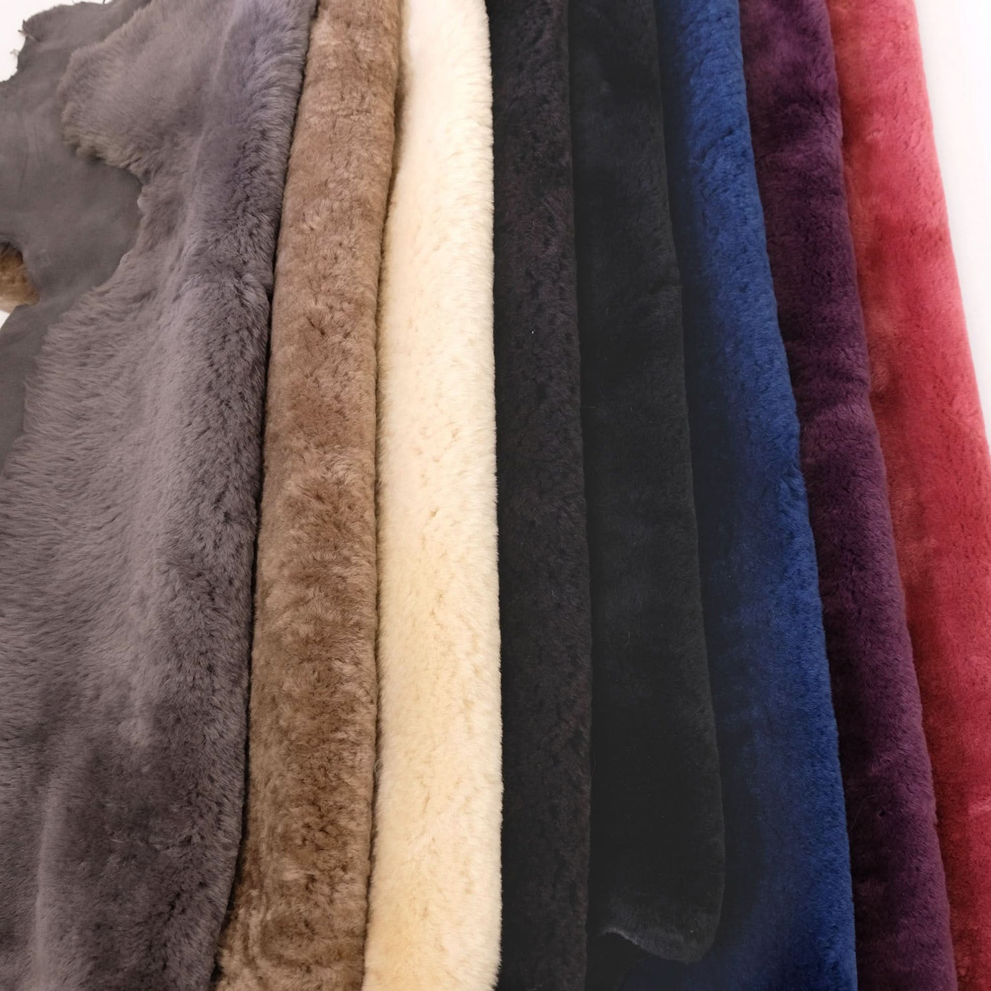 Plush sheepskin rugs in grey, tan, cream, black, blue and burgundy displayed in folded rows. - Yellow Earth Australia